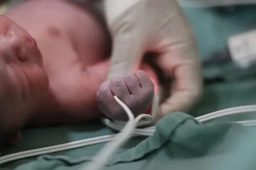 Ручка новорождённого с проводом датчика, рядом рука в медицинской перчатке