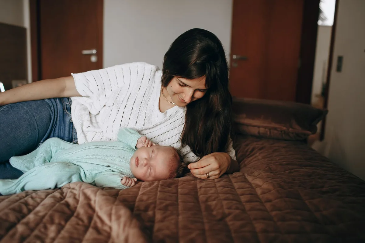 Мама лежит на кровати рядом со спящим новорождённым